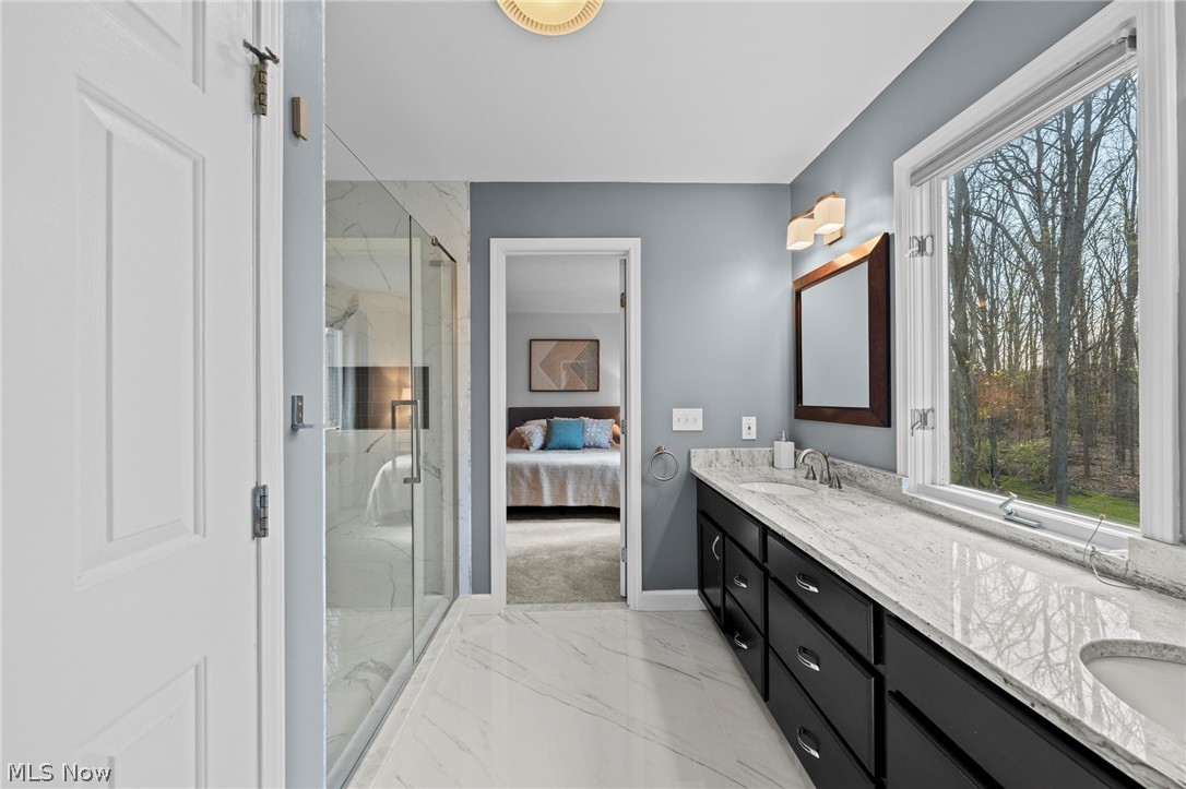 Primary bathroom with marble shower, black vanity, and a large window overlooking trees.