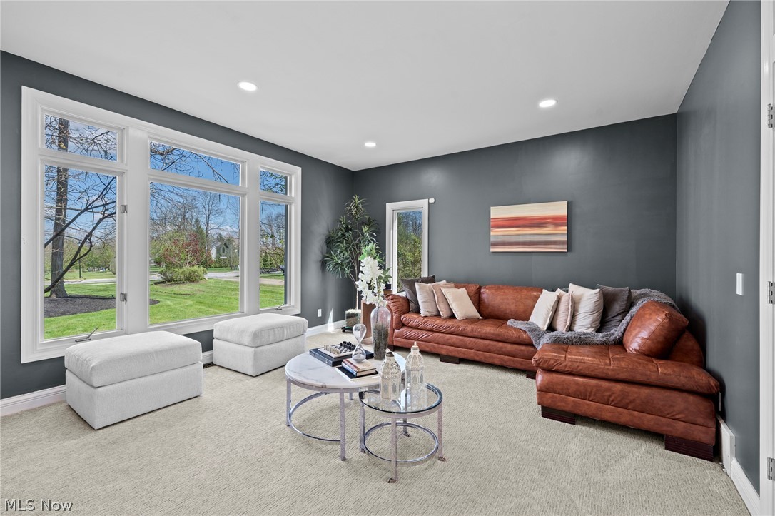 Living room with a brown leather sectional, large windows, and two white ottomans.