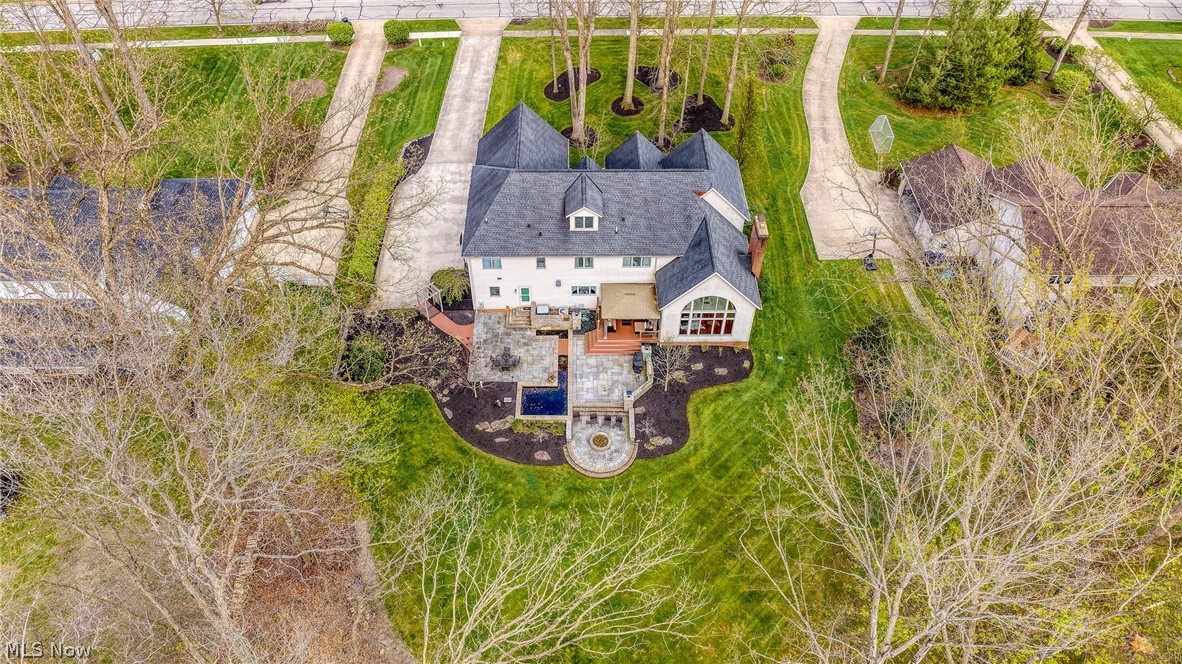 Aerial view of a white house with a stone patio and small pool amid a landscaped lawn.