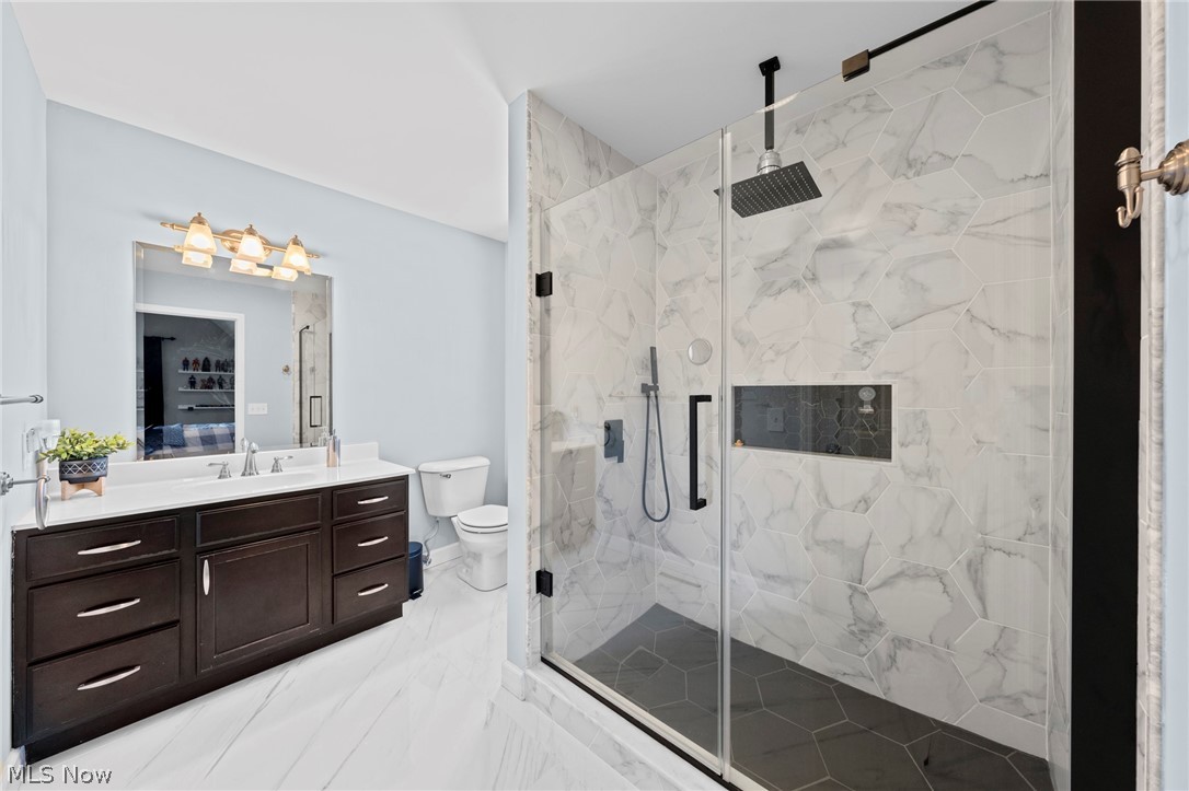 Bathroom with dark double vanity and glass walk-in shower tiled in marble-look hexagons.