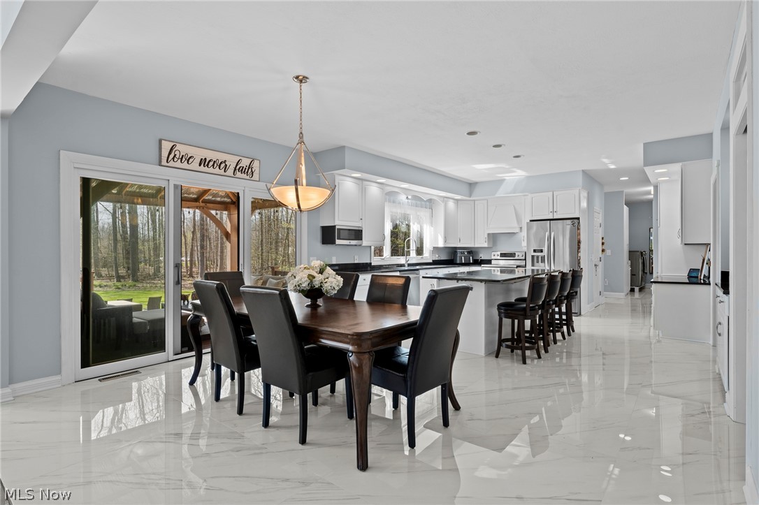Open kitchen and dining area with white cabinetry, marble-look floors, and sliding doors to a wooded backyard.