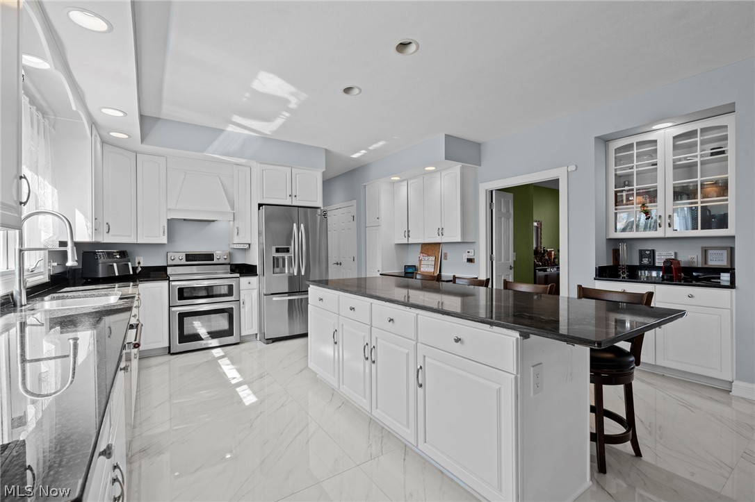 Kitchen with white cabinetry, stainless steel appliances, and a large dark stone island with seating.