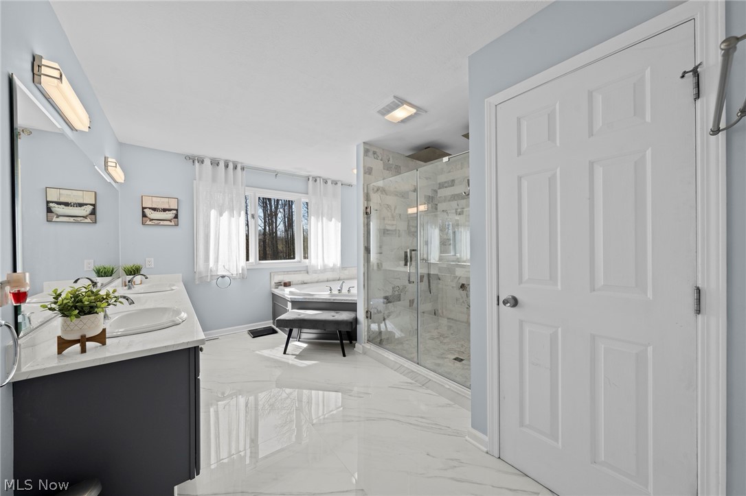 Spacious bathroom with a marble double vanity, soaking tub, glass shower, and glossy marble floors.