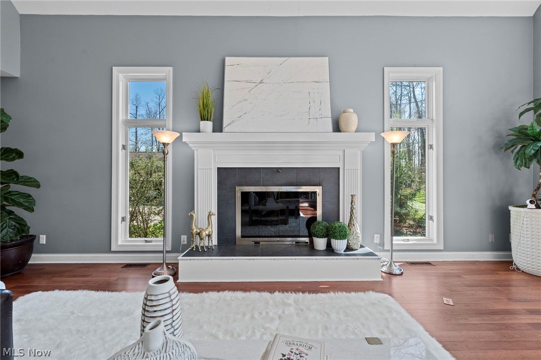 Living room with a white mantel fireplace, dark tile surround, and tall windows overlooking trees.