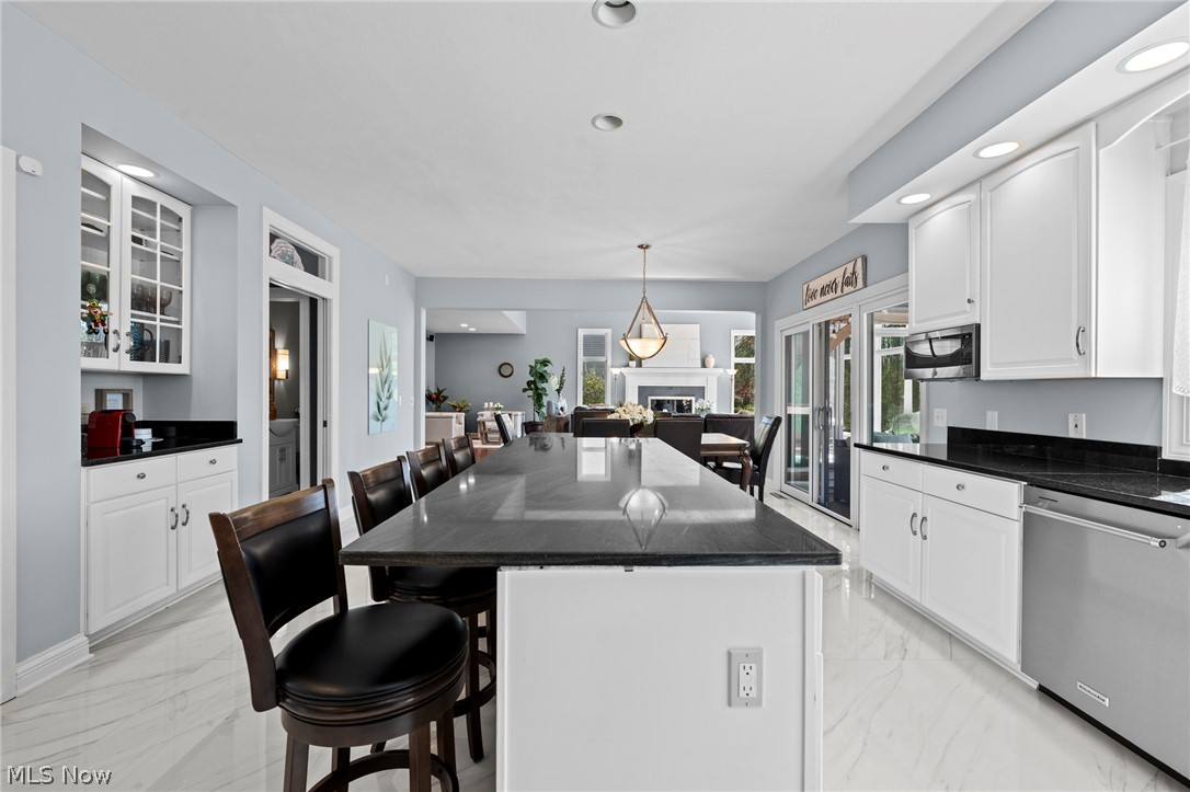Bright kitchen with a large island, white cabinets, marble-look floors, and open dining and living areas.