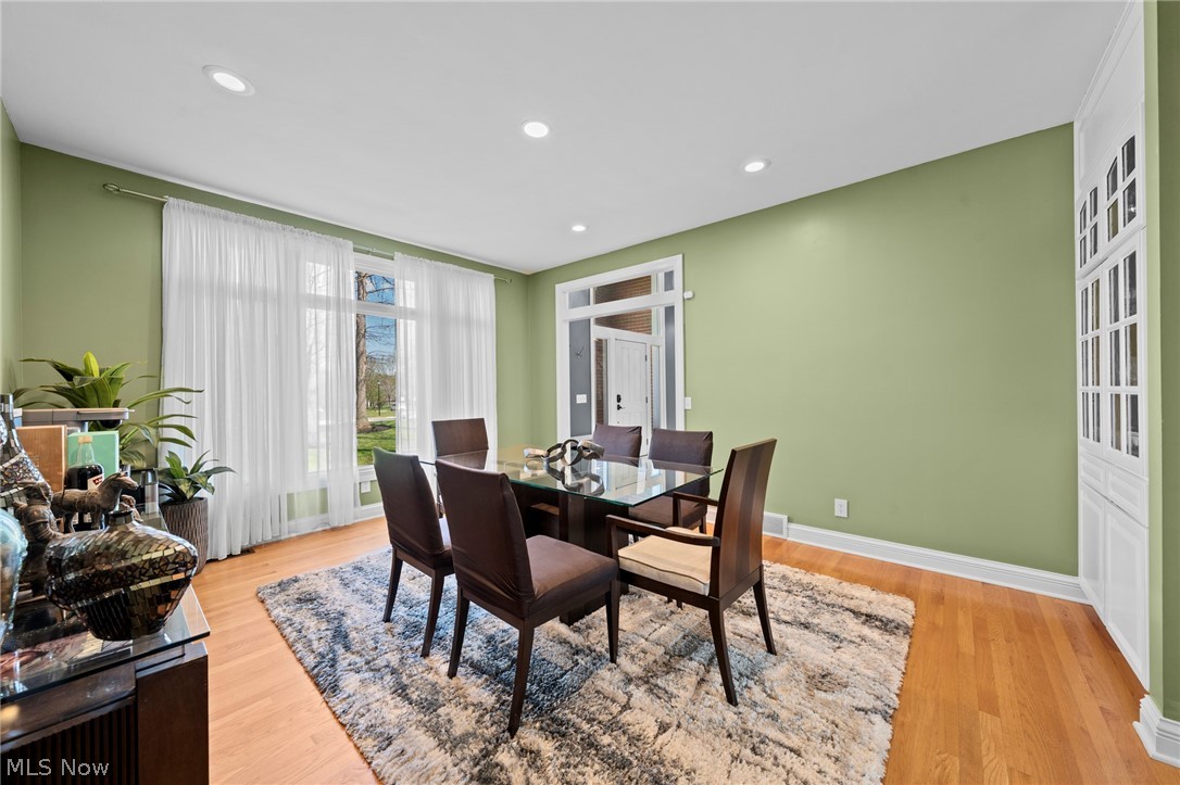 Dining room with sage-green walls, a glass-top table, dark chairs, and tall curtained windows.