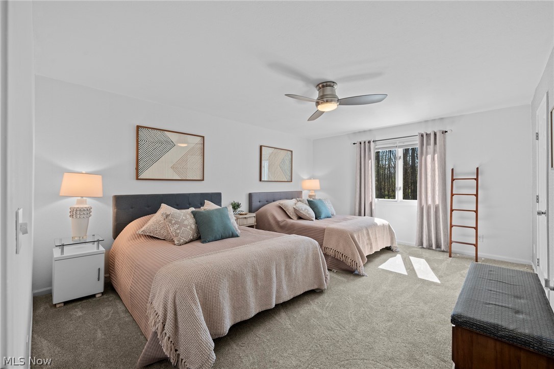 Bedroom with two beds, teal accent pillows, gray carpet, and a window overlooking trees.