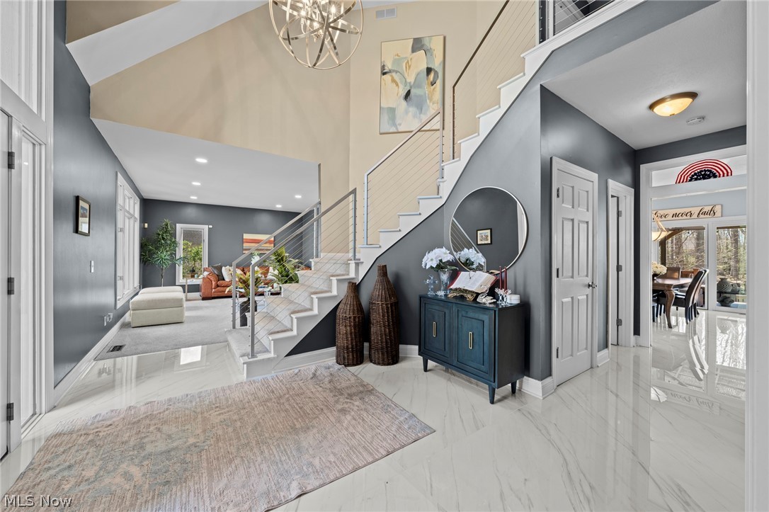 Two-story foyer with a white staircase, glossy tile floors, and a chandelier.