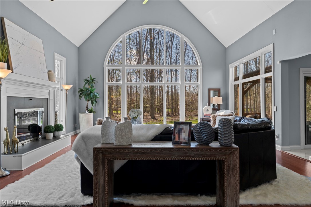 Living room with vaulted ceiling, white fireplace, and arched windows overlooking trees.