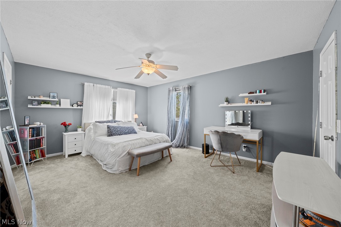 Furnished bedroom with a white bed, gray walls, beige carpet, and a vanity desk.