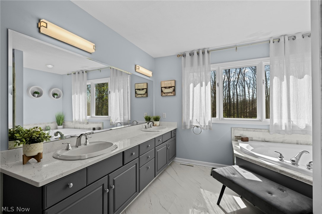 Bathroom with a double-sink vanity, dark cabinets, and a jetted tub beside wooded views.