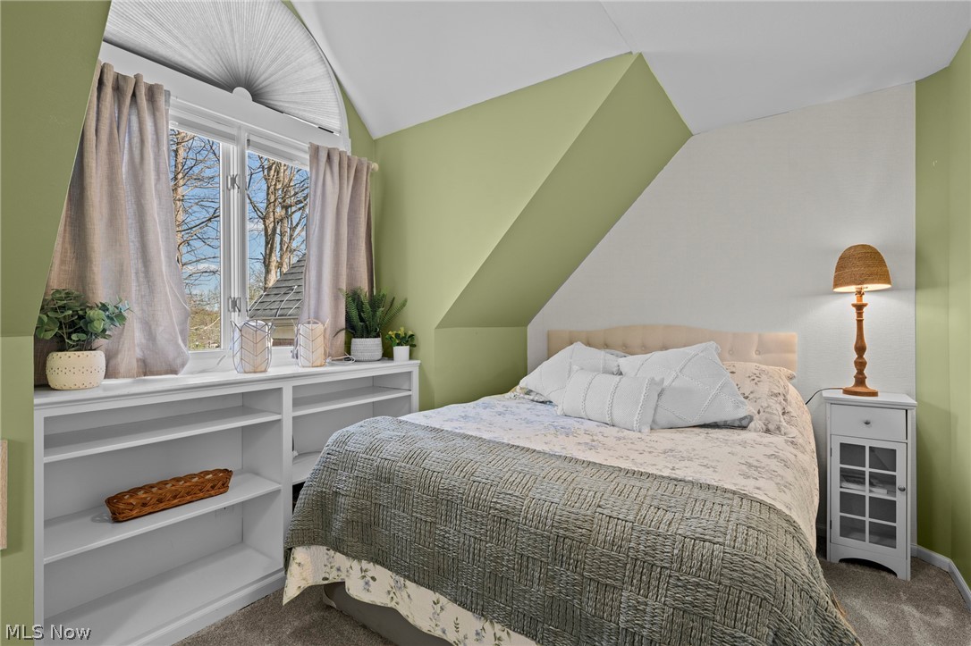 Bedroom with gray quilt, built-in shelves, and a large arched window.