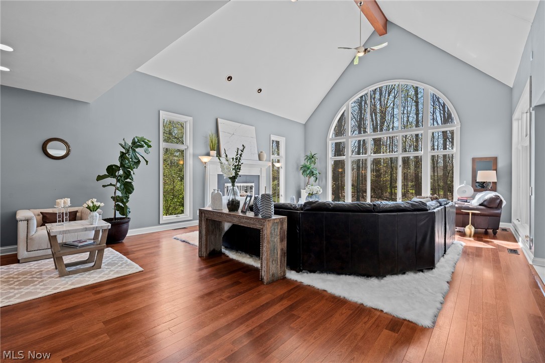 Living room with vaulted ceiling, arched woodland-view window, hardwood floors, and black leather sectional.