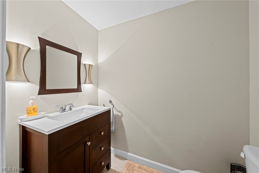 Bathroom with a dark wood vanity, white countertop, large framed mirror, and wall sconces.