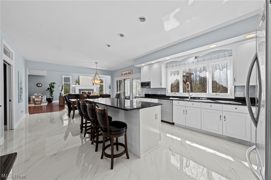 White kitchen with a large black-topped island, bar stools, and windows overlooking trees.