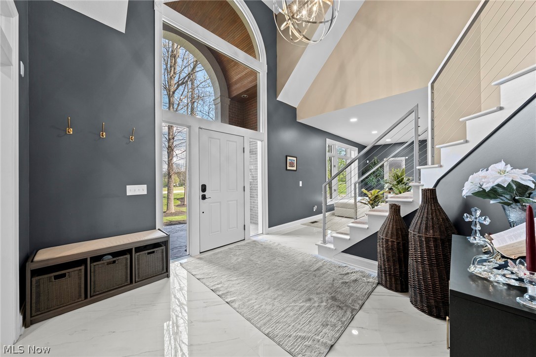 Double-height entry foyer with arched windows, marble-look tile, and a staircase with glass-and-metal railing.