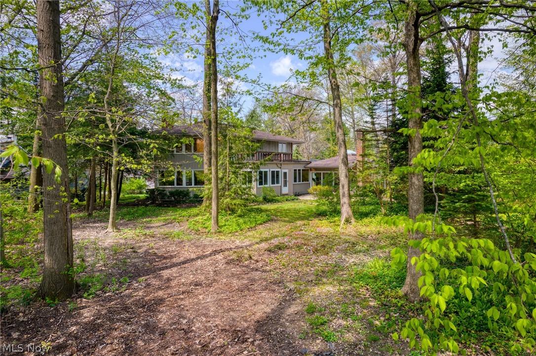 Two-story home with a balcony, seen through trees from a wooded yard.