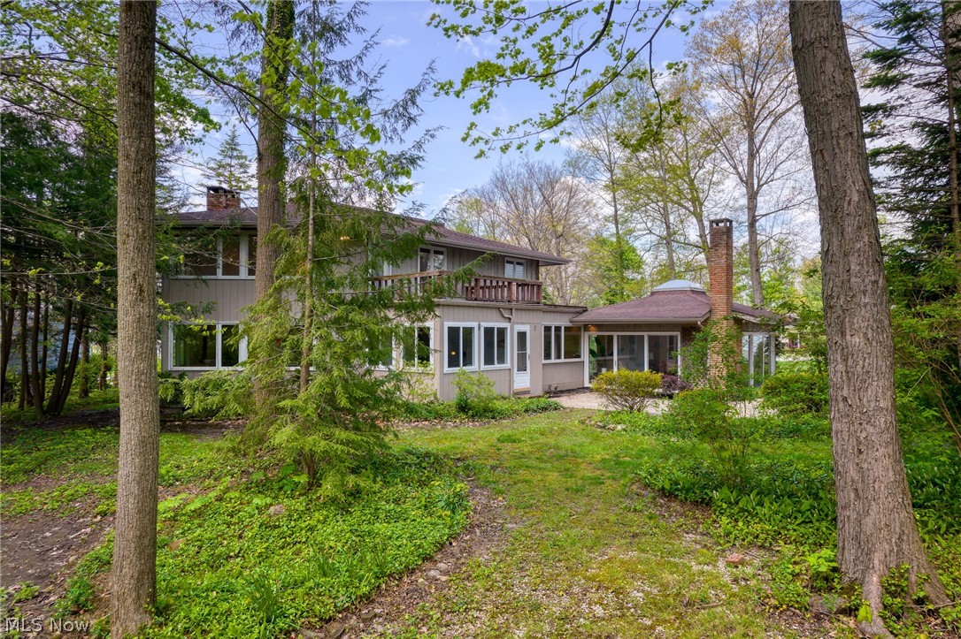 Two-story home with a balcony and brick chimney, surrounded by mature trees and a green yard.
