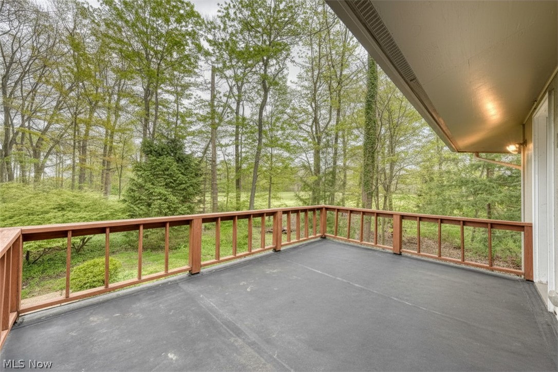 Outdoor deck overlooking leafy trees, with reddish-brown railing and a covered section.