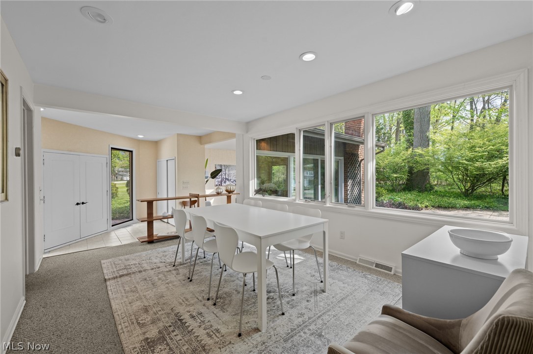 Bright dining room with a white table beside large windows overlooking leafy trees.