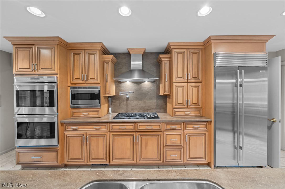 Kitchen with honey-toned wood cabinets, a central cooktop, double wall ovens, and stainless-steel appliances.