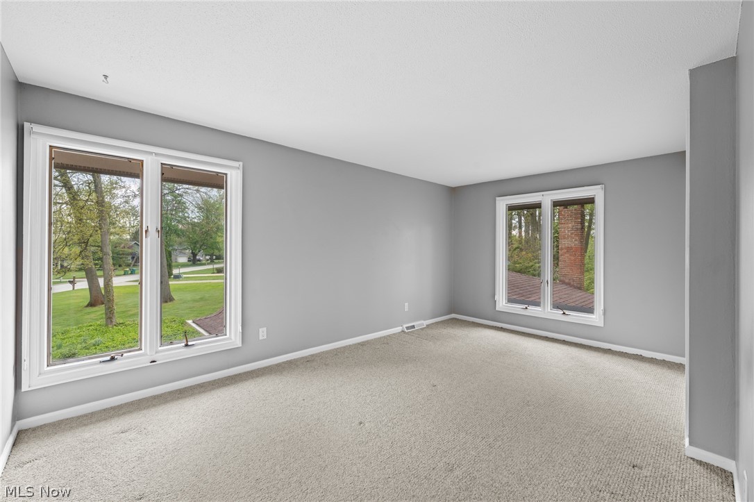 Vacant carpeted bedroom with gray walls and two large windows overlooking the lawn.