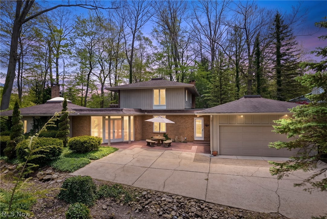 Modern brick-and-gray home with an attached double garage and patio, surrounded by mature trees.