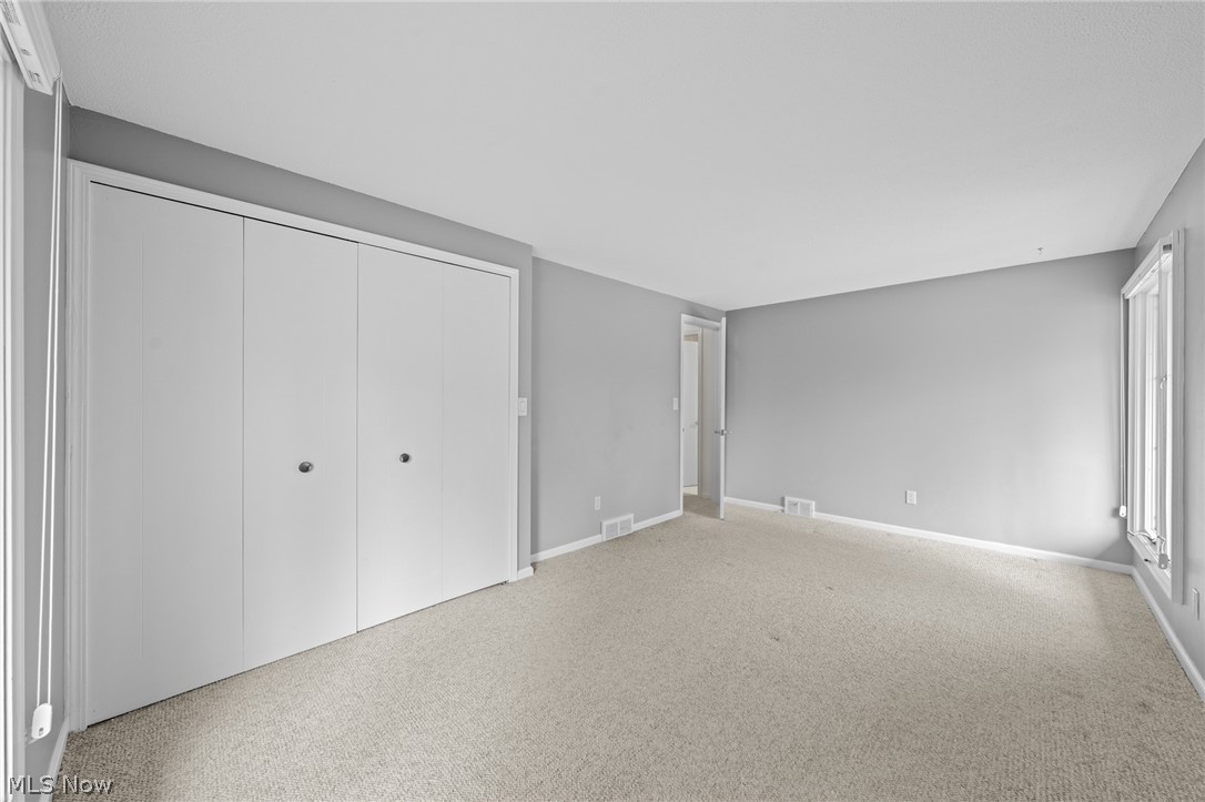Empty bedroom with beige carpet, a large white closet, and tall windows.