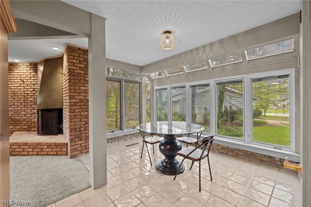 Sunroom with a round glass dining table, expansive windows, and a brick fireplace.
