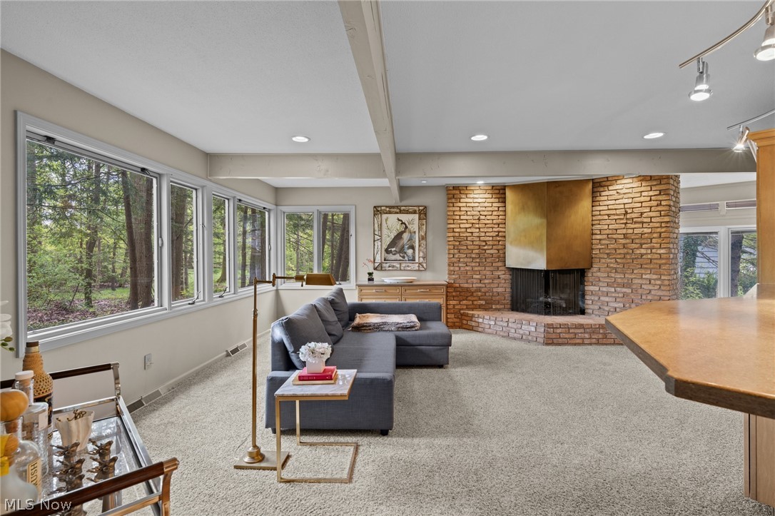 Living room with a gray sectional, brick fireplace, and large windows overlooking trees.