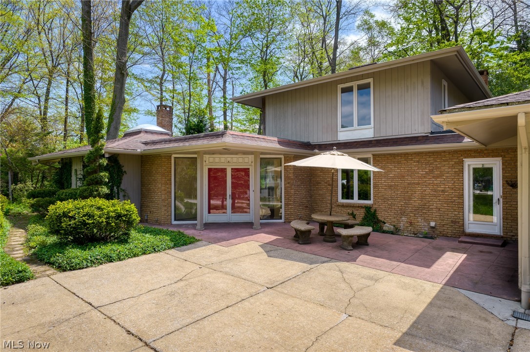 Rear of a brick and wood-sided home with a paved patio and umbrella-shaded seating.