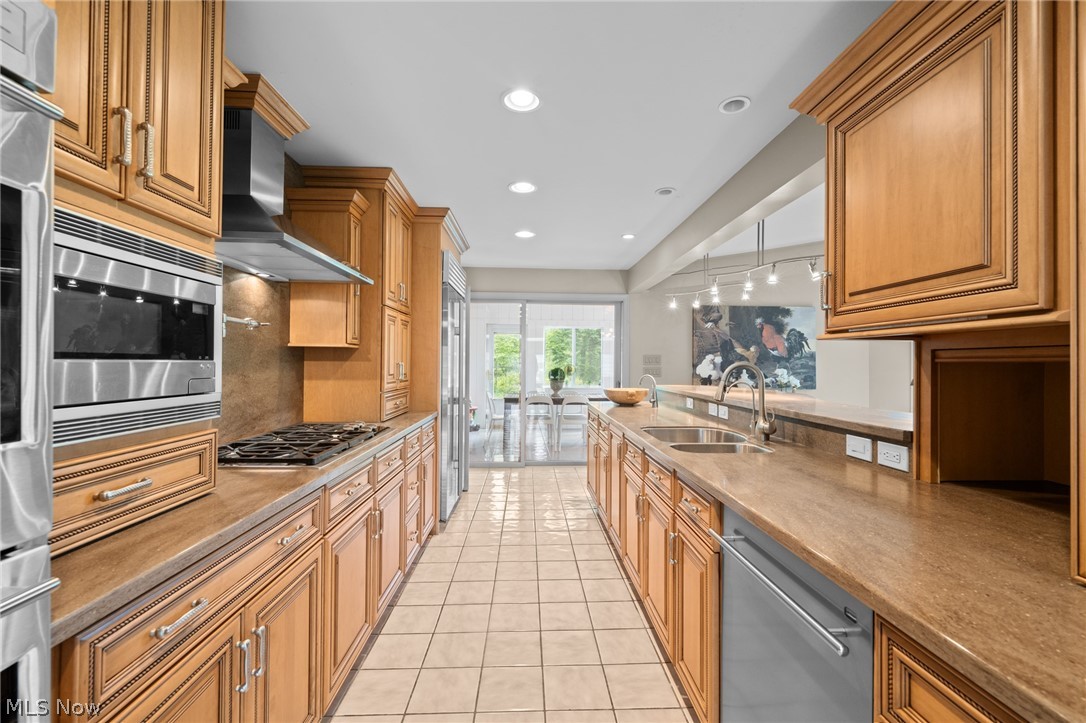 Kitchen with honey-colored wood cabinets, stone counters, stainless steel appliances, and a dining area beyond.