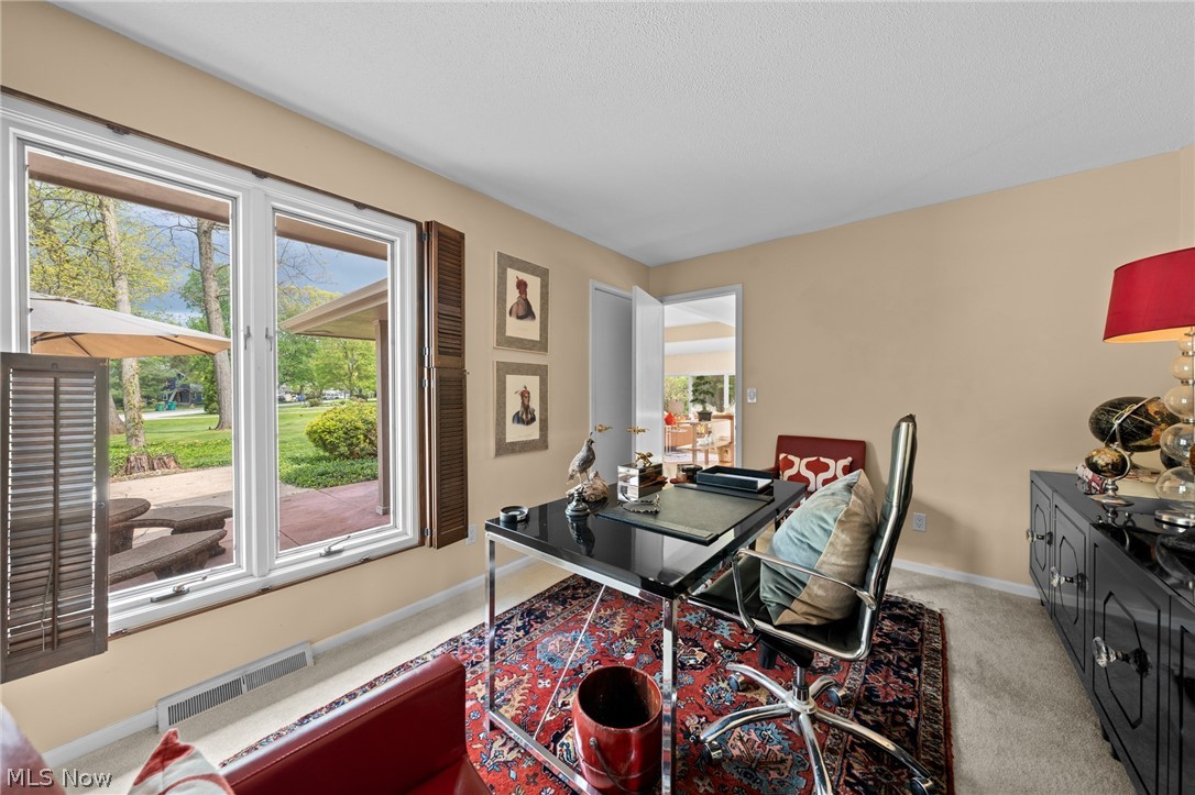 Furnished home office with a glass desk and large windows overlooking a leafy lawn.