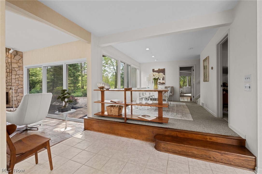 Open living and dining area with a stone fireplace, broad windows, and a raised wood platform.