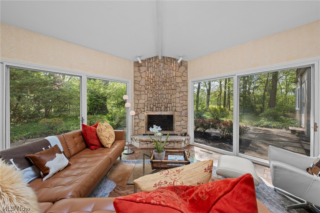 Living room with a stone fireplace, leather sofa, and large windows overlooking a wooded yard.