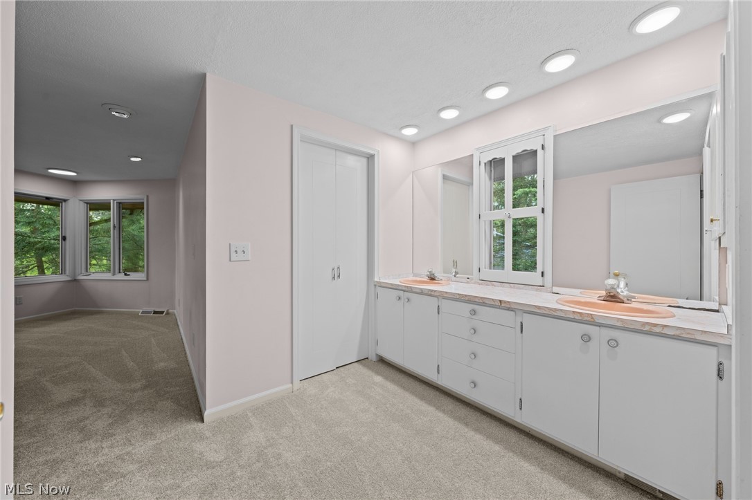 Bathroom with a long double-sink vanity and an adjoining carpeted room with bay windows.