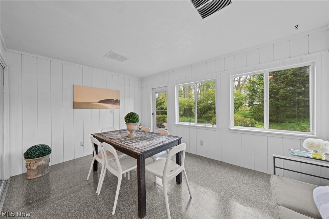 Dining area with a dark wood table, white chairs, and large windows overlooking trees.