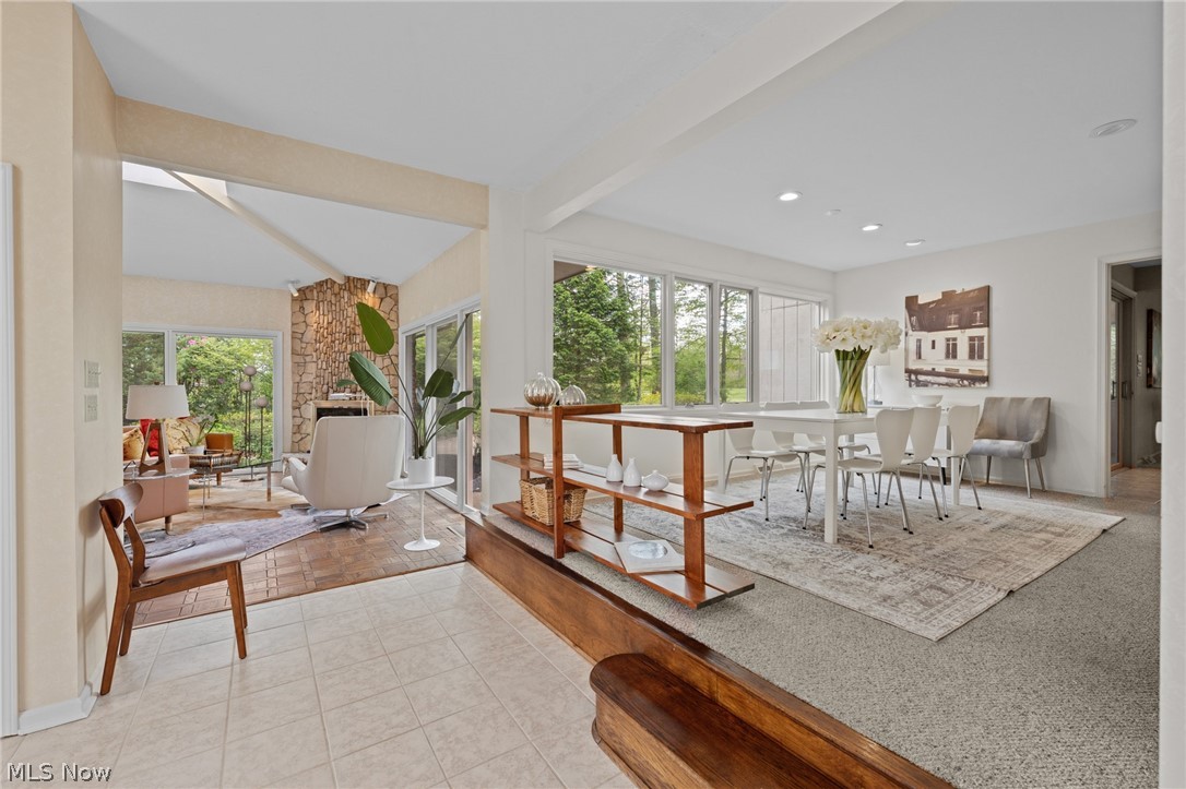 Open living and dining area with large windows, furnished seating, and a stone fireplace.
