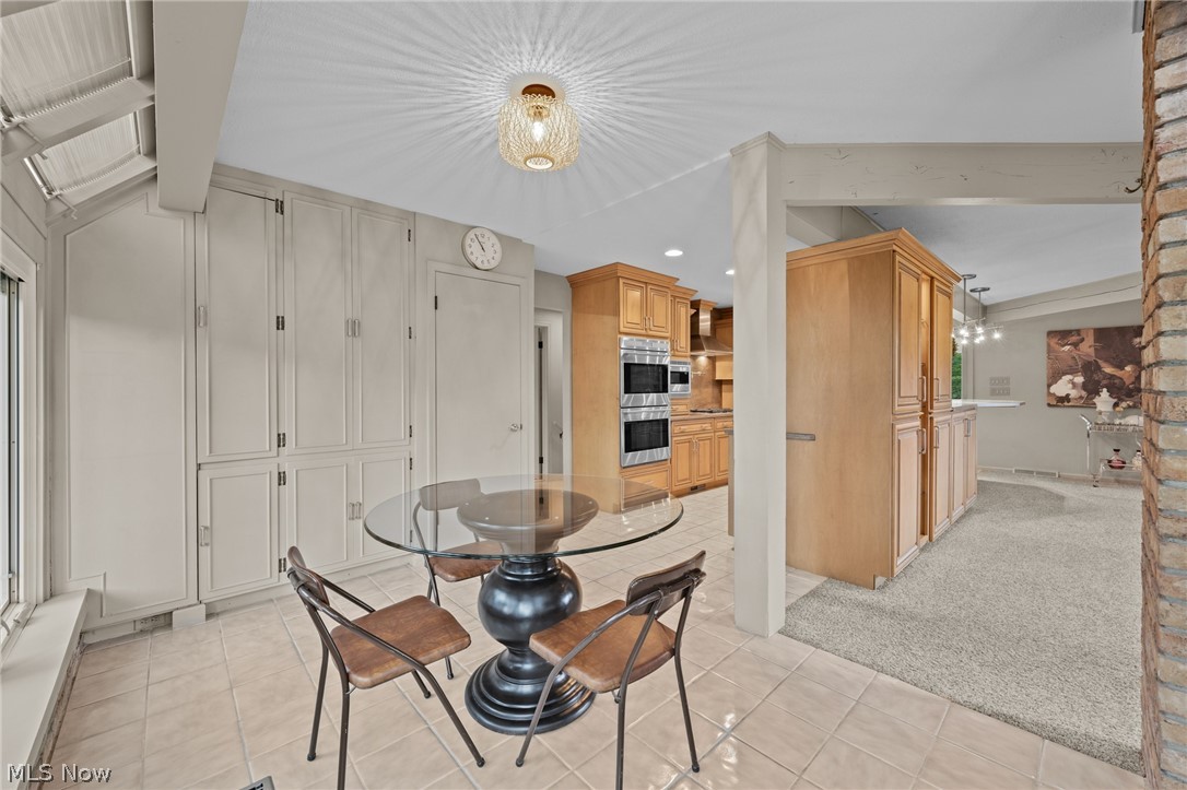 Kitchen and breakfast area with a glass dining table, white built-ins, and warm wood cabinetry.