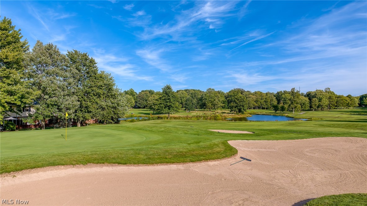 Golf course with a flag-marked green, foreground sand bunker, and pond.