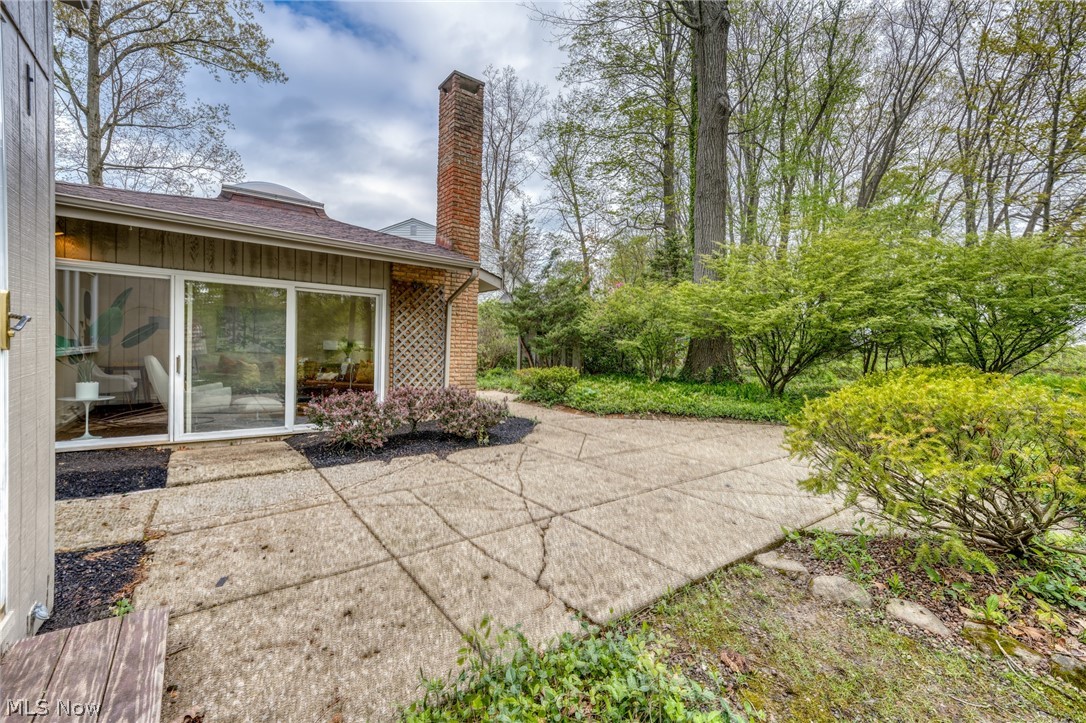 Concrete patio beside sliding glass doors, a brick chimney, and landscaped shrubs.