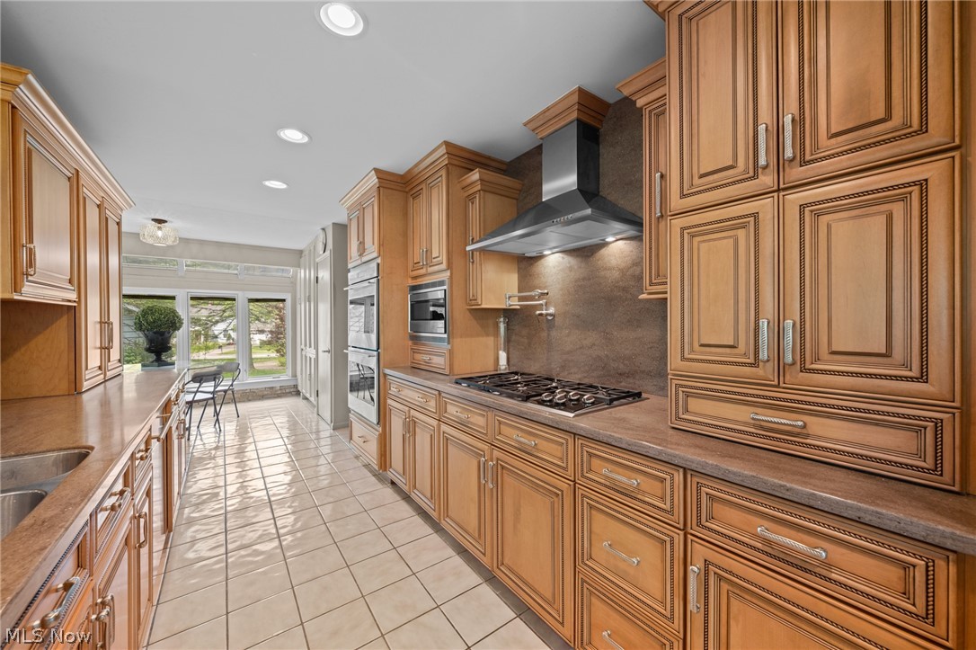 Galley kitchen with ornate wood cabinets, a gas cooktop, double ovens, and a bright windowed dining area.