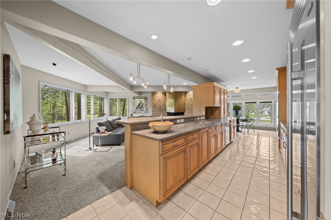 Open-plan kitchen with a long wood-cabinet island, brick backsplash, and adjoining living area beside large windows.