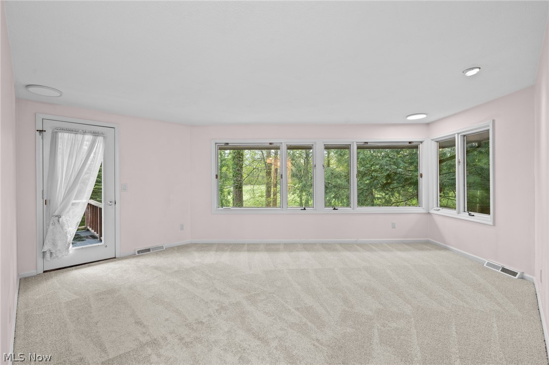 Empty carpeted room with wide windows overlooking trees and a glass door to a deck.