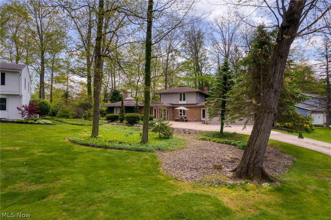 Two-story brick home framed by mature trees, with a broad lawn, patio, and driveway.