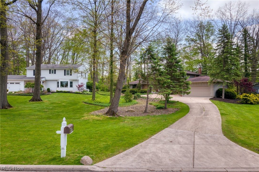 White two-story home among mature trees, with a curved driveway and front lawn.