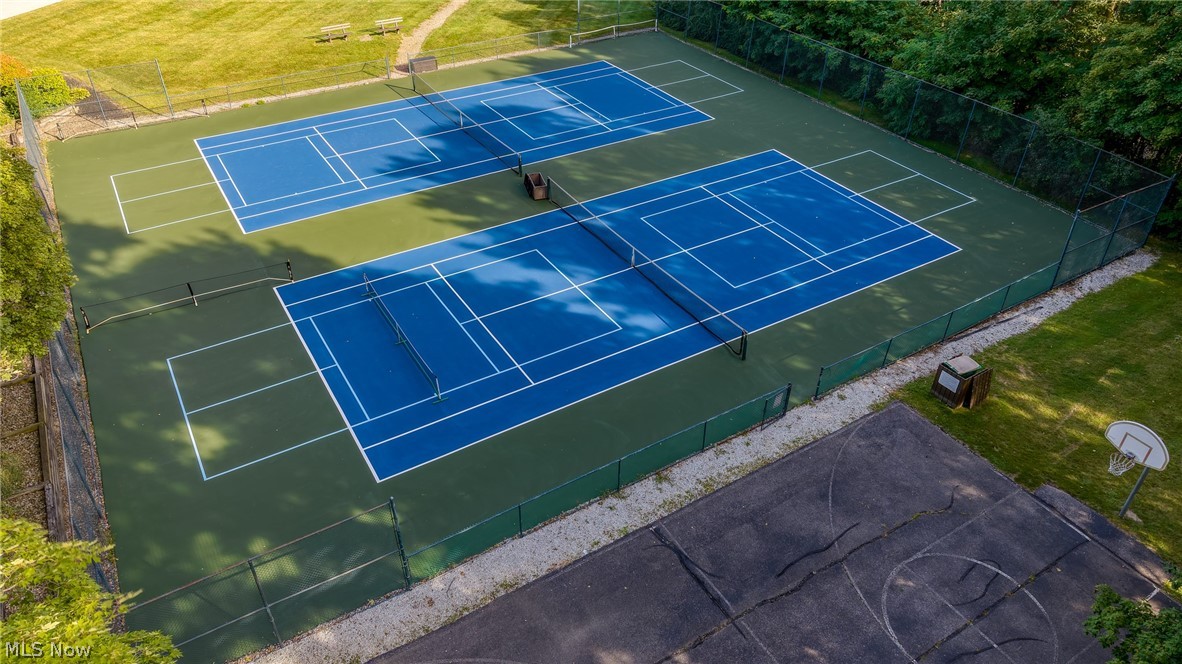 Two blue tennis courts beside a basketball court, surrounded by fencing and trees.