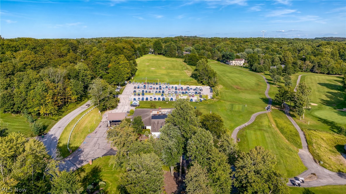 Aerial view of a tree-lined golf course, winding cart paths, parking lot, and clubhouse.