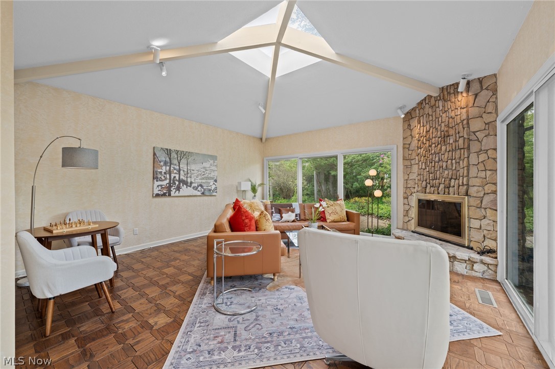 Living room with a vaulted skylight ceiling, stone fireplace, and large windows facing greenery.