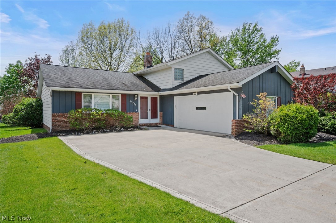 Blue-and-white split-level home with brick accents, red front door, and wide concrete driveway.